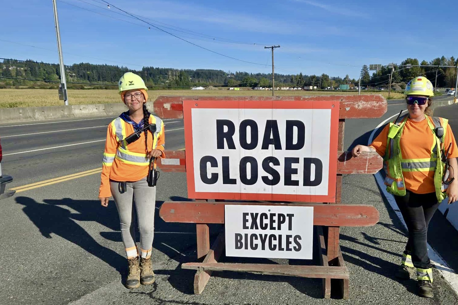 Construction workers stand next to a 'Road closed' sign