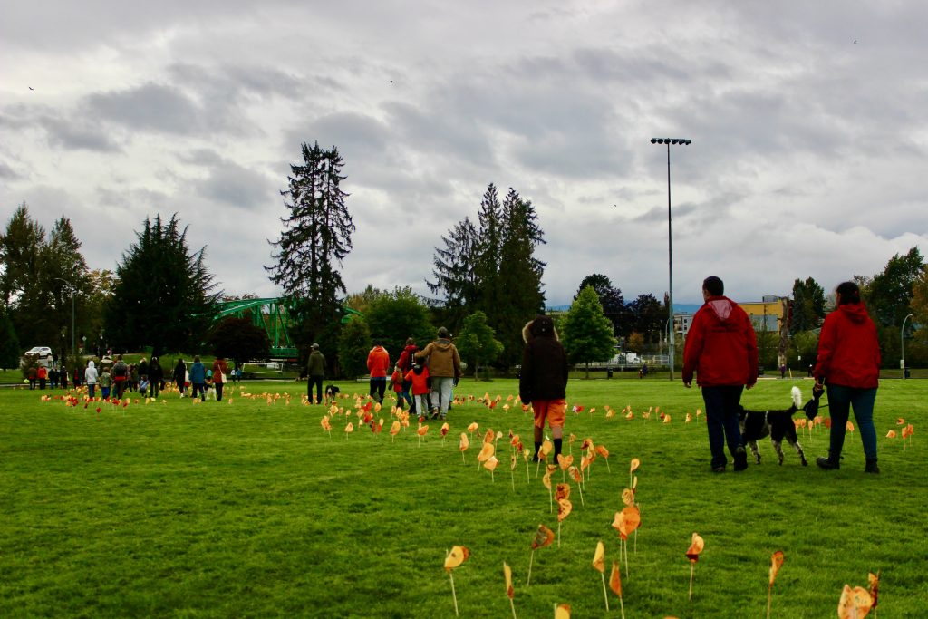 A line of people walk along a path marked by orange paper hearts. It is cloudy out. 