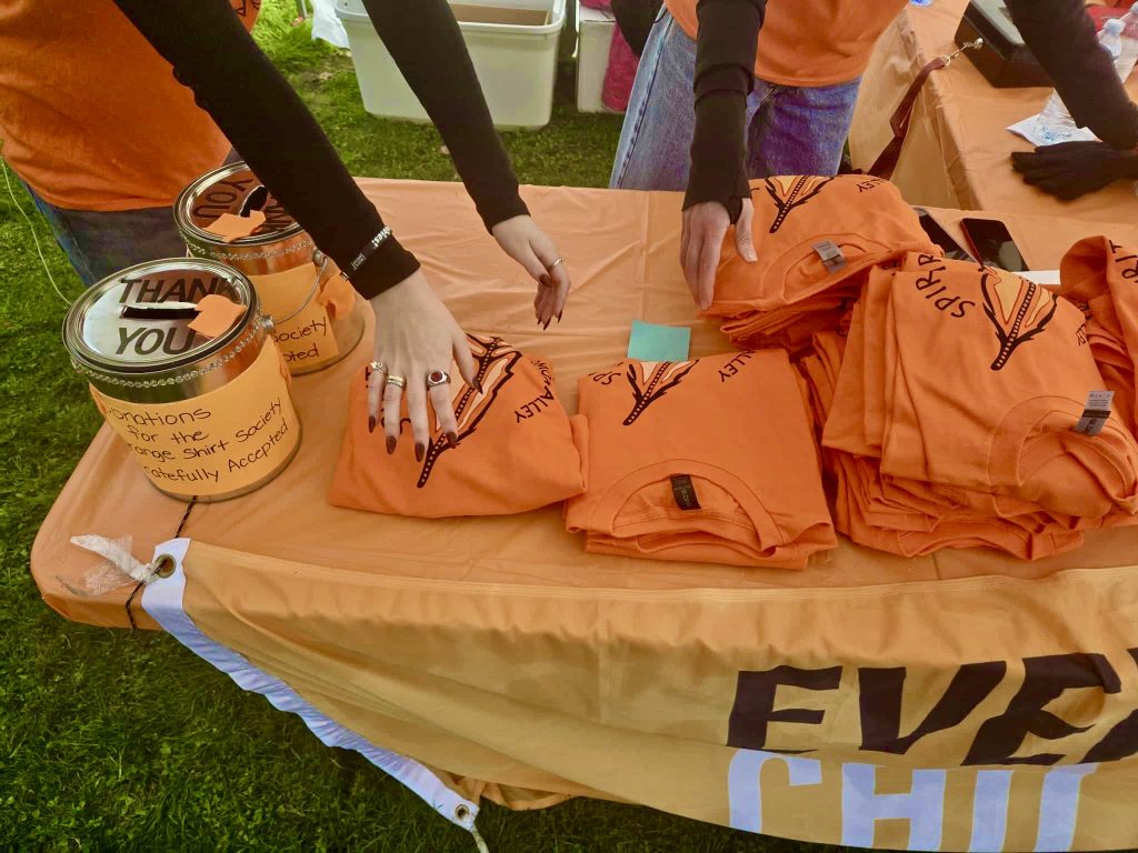 Orange shirts folded on a table with someones hands in the image, appearing to be organizing the shirts.