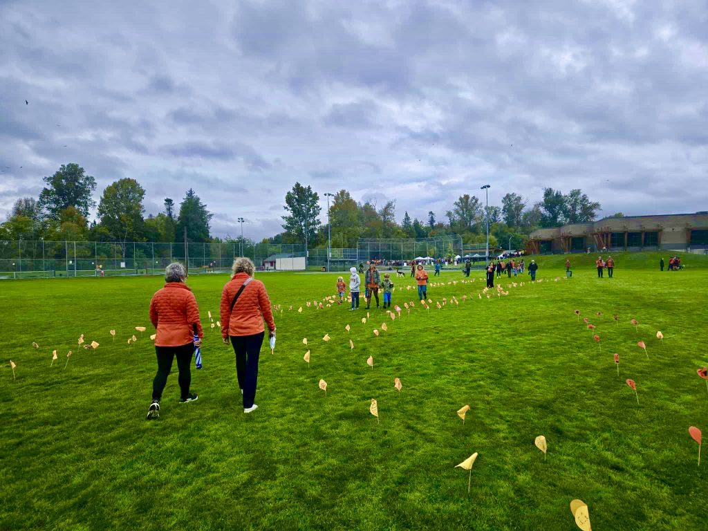 Two women in orange jackets walk along a path market by orange paper hearts.
