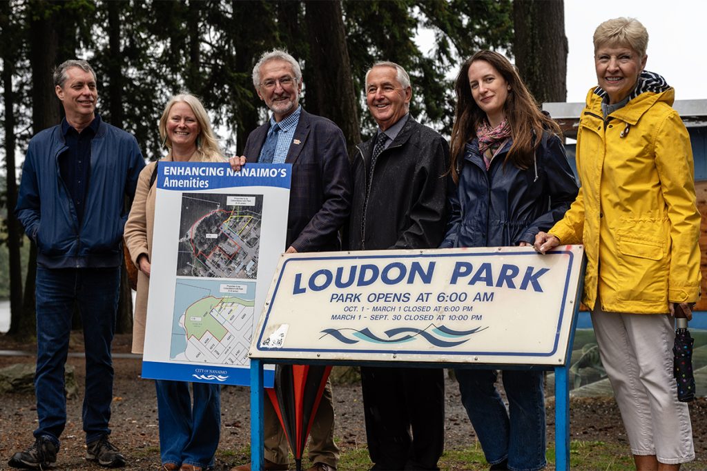 Nanaimo city council members pose for a photo by the Loudon Park sign after a press conference announcing the expansion of the park on Wednesday, Oct. 1, 2025. From left to right: Councillors Paul Manly and Erin Hemmens, Mayor Leonard Krog, Councillors Ian Thorpe, Hilary Eastmure and Janice Perrino. Photo by Mick Sweetman / The Discourse.