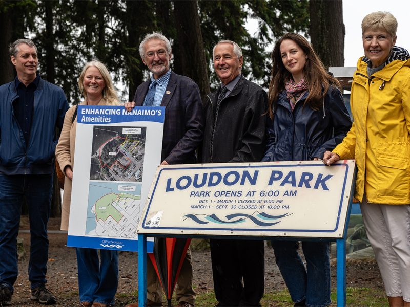 Nanaimo city council members pose for a photo by the Loudon Park sign after a press conference announcing the expansion of the park on Wednesday, Oct. 1, 2025. From left to right: Councillors Paul Manly and Erin Hemmens, Mayor Leonard Krog, Councillors Ian Thorpe, Hilary Eastmure and Janice Perrino. Photo by Mick Sweetman / The Discourse.