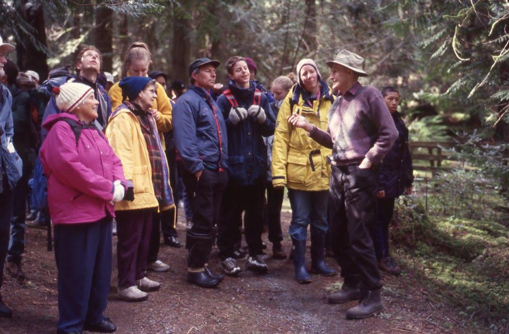A photo of a man talking to a group of people on a trail in the forest