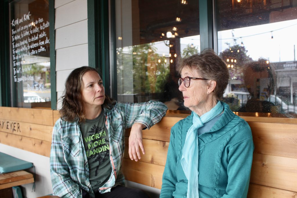 Two women sit on a bench outside having an engaged conversation.