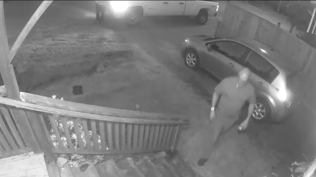 A screenshot of a black and white video of a man about to walk up steps to the front of a home.