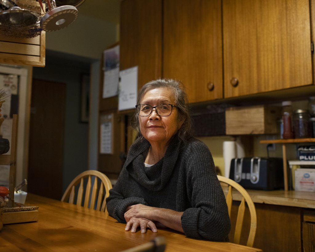Josephine Andrew, mom of an Indigenous teen who was stabbed in Courtenay, B.C., sits at a table in her home looking into the distance with a stern expression.