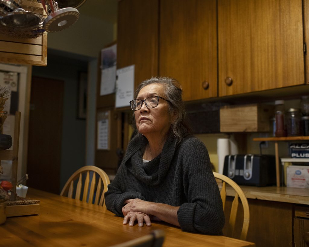 Josephine Andrew, mom of an Indigenous teen who was stabbed in Courtenay, B.C., sits at a table in her home looking into the distance with a stern expression.