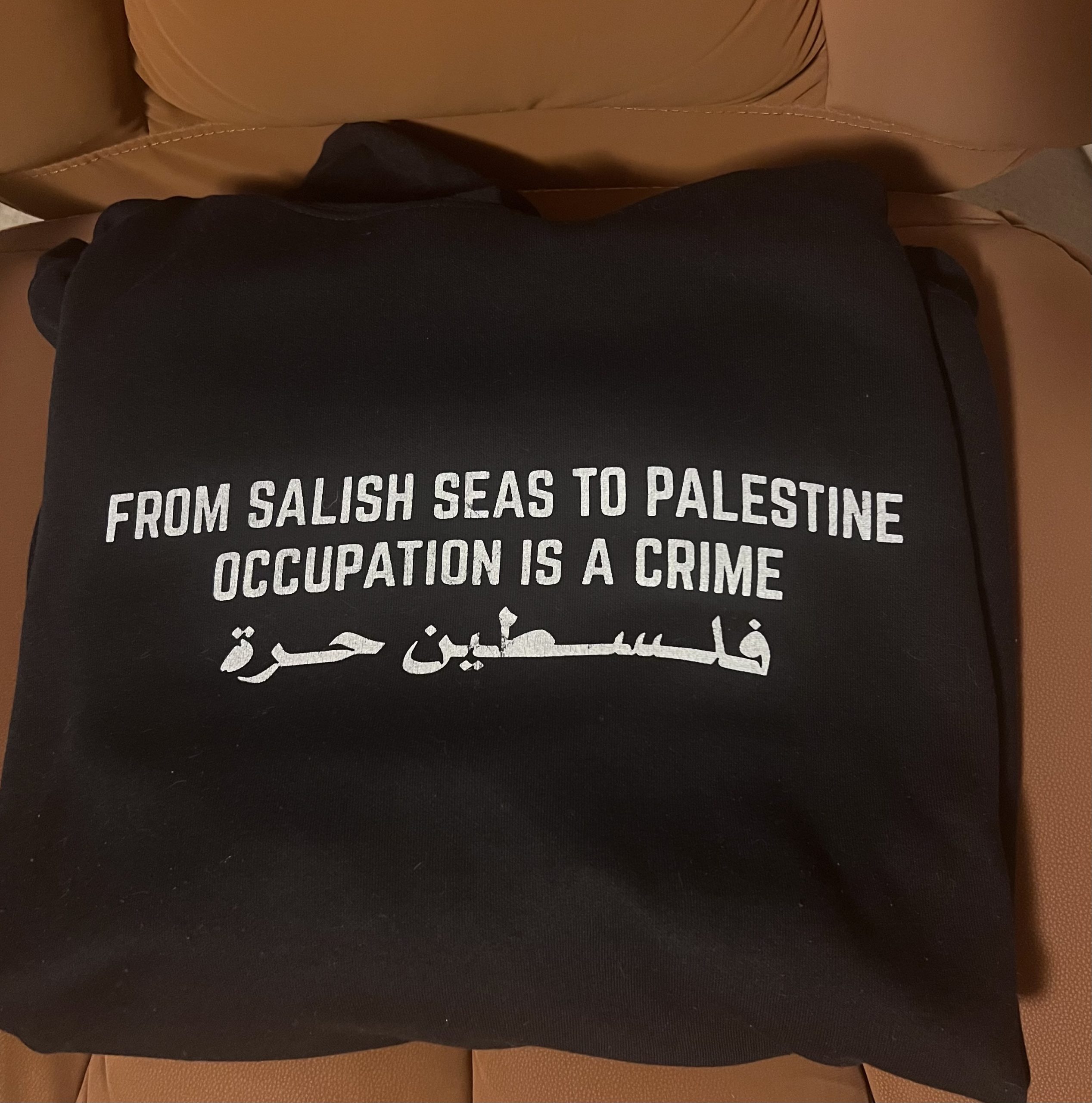A black shirt that says 'From Salish Seas to Palestine Occupation is a Crime', worn by Blondeau to the public town hall in Duncan.