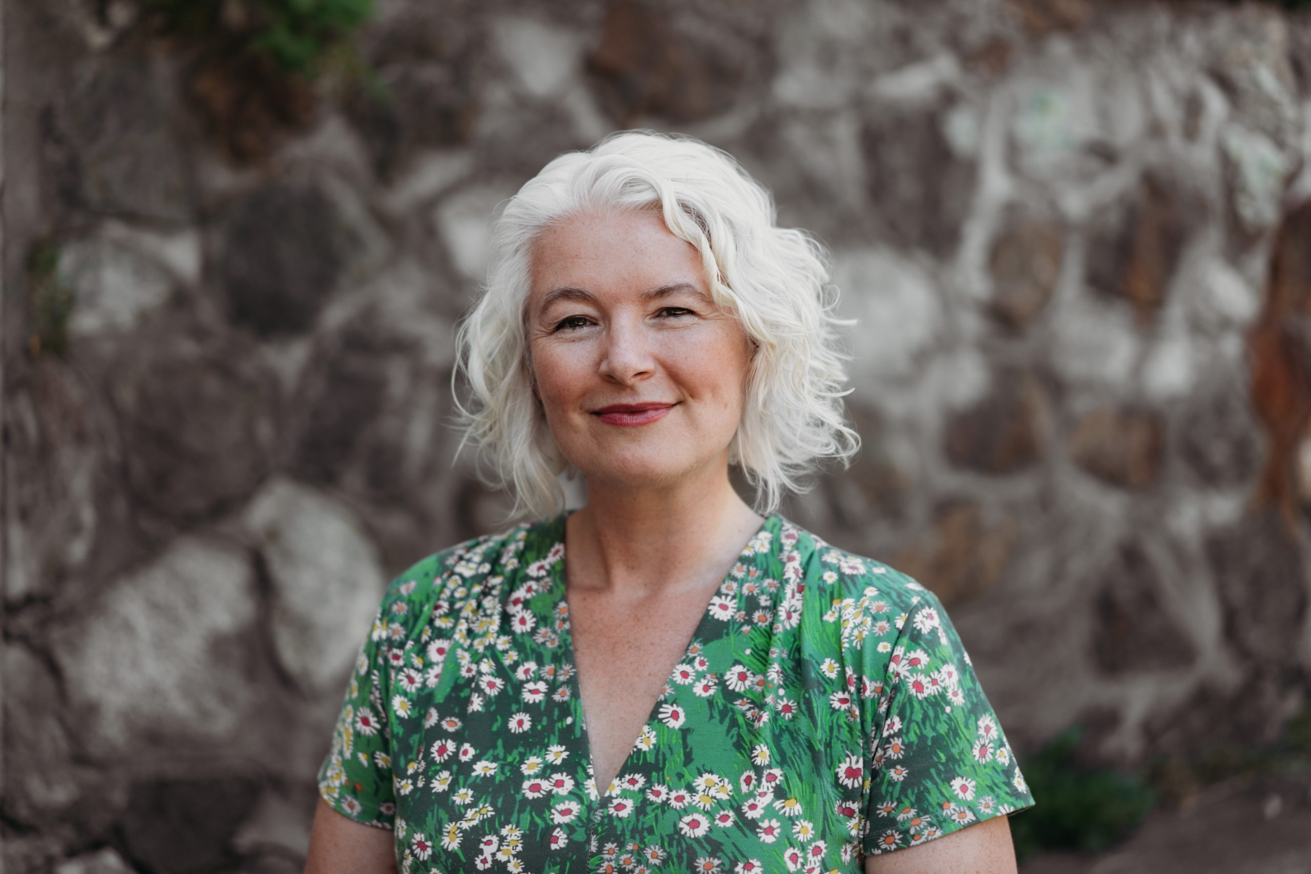 A photo of writer Zena Sharman standing infront of a stone wall.