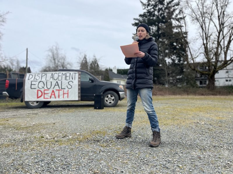 Alex Schiebel of the Cowichan Community Care Network speaks at a rally in front of banners.
