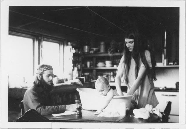 A black and white photo of a young couple bathing a baby in a small tub on a table.