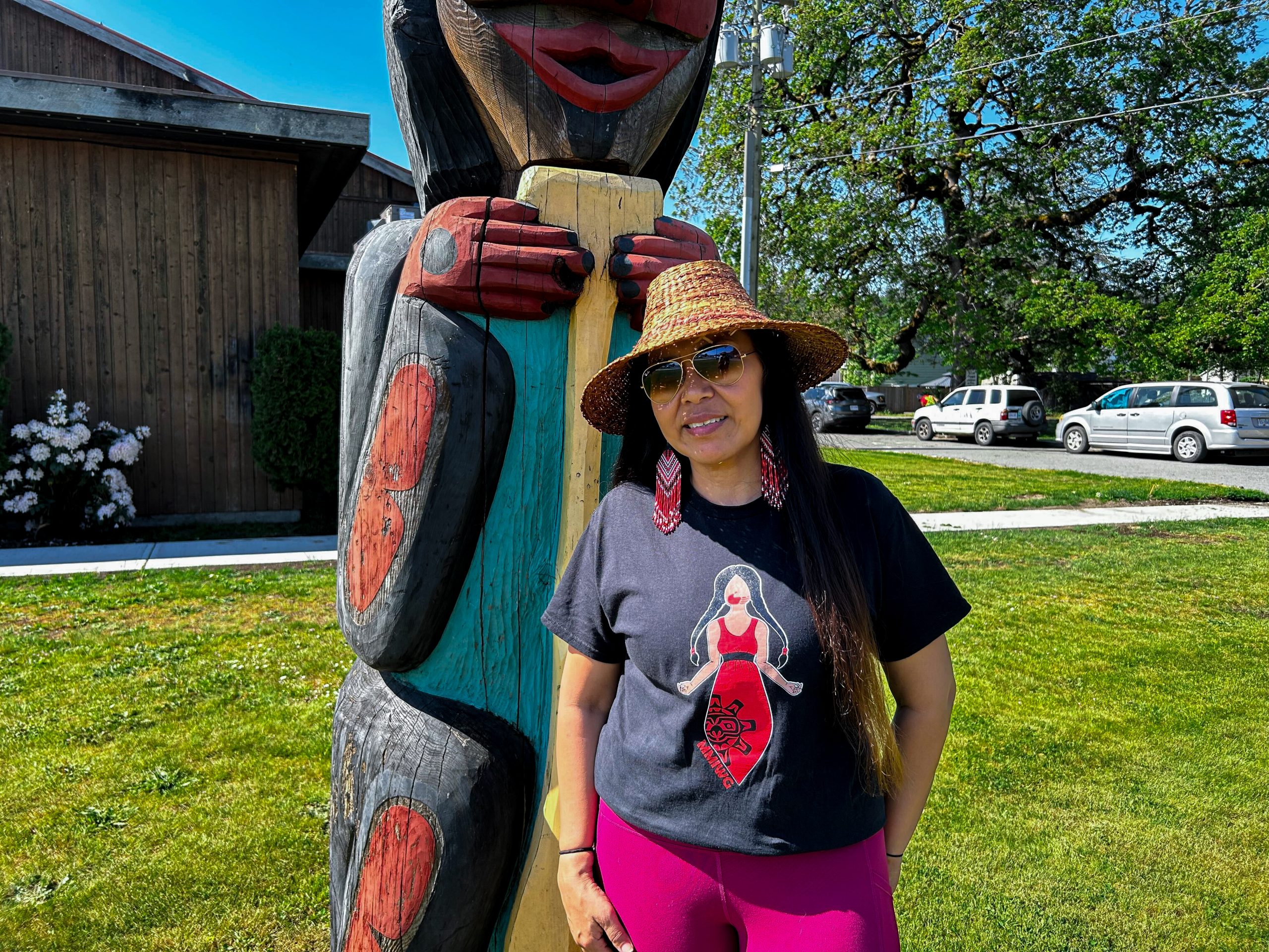 A photo of LuuGakk’ (Liza Haldane) in front of a totem pole.