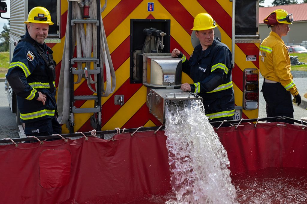 Bart Rosser (left) is a captain with the Cranberry Volunteer Fire Department and has been deployed to a number of severe wildfires in B.C.’s interior. He brought his experience to a joint training exercise with local fire departments at the Nanaimo Military Camp on May 9, 2026. Firefighter Petr Dratva (right) helps fill a large container with water from the department’s tender. Photo by Mick Sweetman / The Discourse.