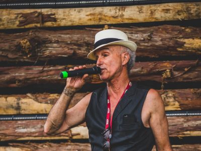 Avigdor Schulman, known to have supported the music scene in Cumberland, speaks holding a microphone while wearing a black leather vest and white and black fedora.
