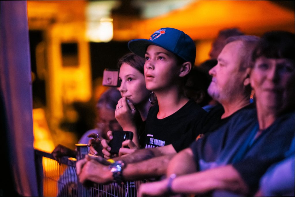 Young audience members stand behind a concert barricade seemingly mesmerized by what they're looking at