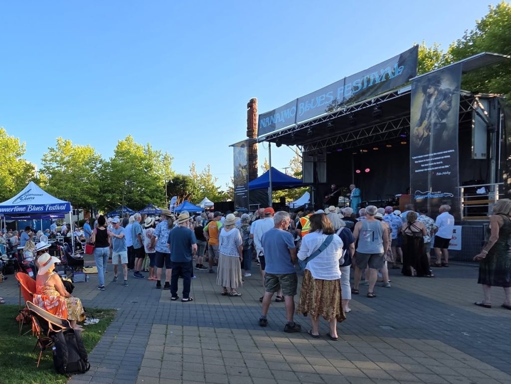 A crowd of Nanaimo Blues Festival goers stands in front of a stage at Maffeo Sutton Park