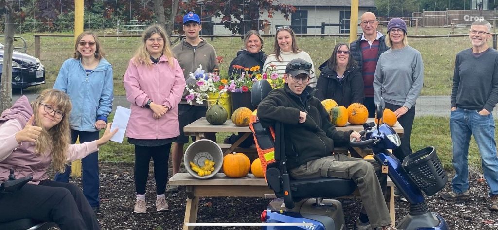A group of smiling adults situated around a table with pumpkins on it.