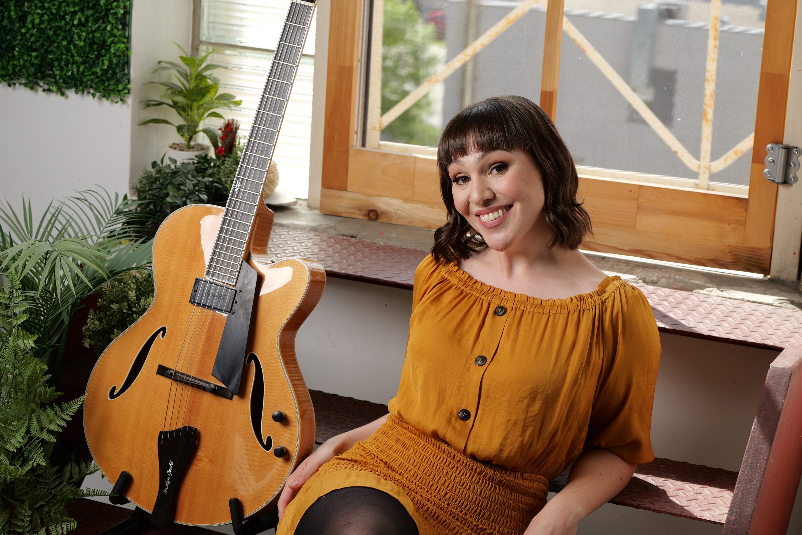 A headshot of Jocelyn Gould sitting next to a guitar