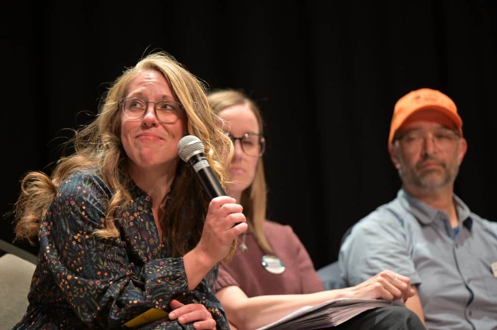 Nanaimo mayor candidate Sarah Lovegrove holds a microphone to her face while seated on a stage next to other council candidates.