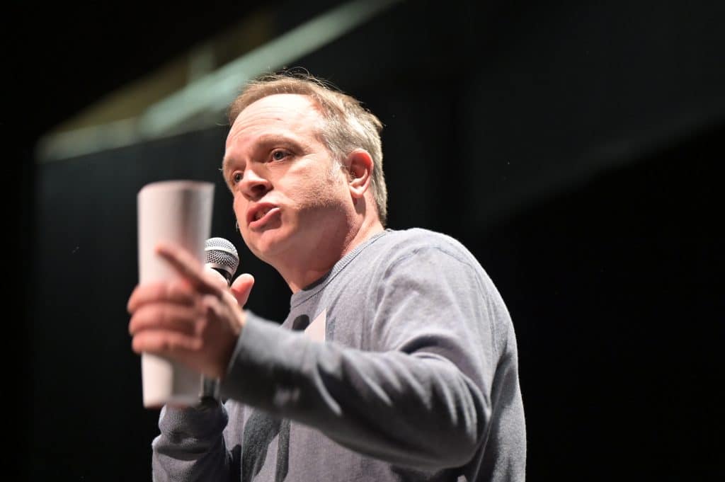 Jeff Annesley, council candidate, speaks passionately into a microphone while holding a rolled up paper in his other hand.