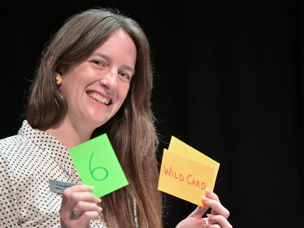 Current Nanaimo Councillor Hilary Eastmure smiles and holds up two cards in her hands. One card has the number six on it and the other says "wild card" on it.